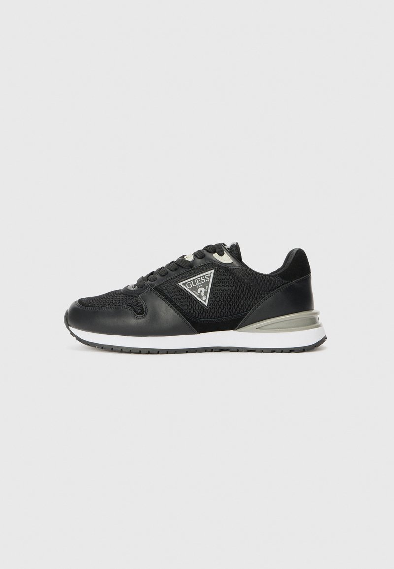 Black sneaker with mesh and leather material, featuring a triangular logo, contrasting white sole, and lace closure with reinforced eyelets.
