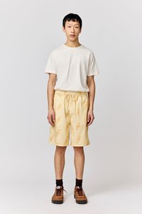 Light yellow shorts with fish pattern, elastic waistband, and drawstring; styled with a plain white t-shirt and brown sneakers.