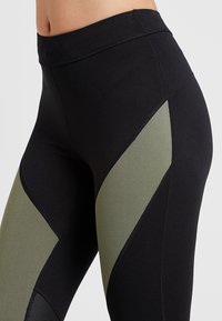 Leggings taille haute avec des panneaux noirs et vert olive. Conçus en tissu extensible avec une texture lisse et des coutures contrastées.