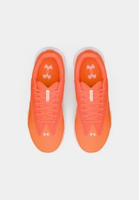 Jasnopomarańczowe buty sportowe Under Armour z sznurówkami, widziane z góry na białym tle.