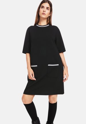 Schwarzes Kleid mit kurzen Ärmeln, runder Ausschnitt, verziert mit weißen gewellten Säumen und zwei Fronttaschen mit kontrastierenden gestreiften Details.