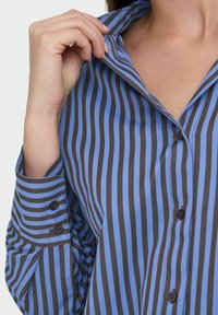 Chemise à boutons avec des rayures verticales bleues et marron, un col pointu et des poignets à boutons, fabriquée à partir d'un tissu lisse.