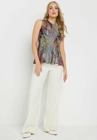 Blusa senza maniche a fantasia floreale in tessuto morbido e trasparente con dettagli plissettati. Abbinata a pantaloni bianchi a gamba larga e scarpe bianche.