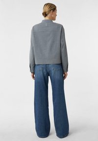 Szara krótka kurtka z prostym kołnierzem, długimi rękawami i poziomym szwem z tyłu, zestawiona z szerokimi niebieskimi dżinsami.