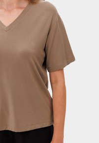 Hnědý krátký rukáv V-čkový tričko z měkké tkaniny, s uvolněným střihem a lemováním, které se mírně zakřivuje nahoru na bocích.