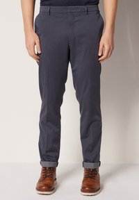 Mörkblå, rakpassade chinos med en slät textur. Har sidfickor, bälteshällor och uppvikta benslut. Kombineras med bruna snörkängor.