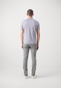 T-shirt corta a maniche corte di colore viola chiaro con una vestibilità regolare, abbinata a pantaloni slim-fit grigio chiaro e sneakers bianche, vista dal retro.