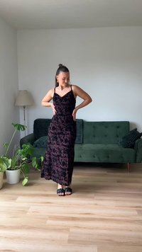 Svart maxi-kjole i fløyelsstoff med blomstermønster, tynne stropper, tettsittende silhuett og en sideslitt. Brukt med svarte sandaletter.