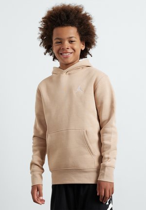 Felpa beige con cappuccio e tasca frontale, logo bianco sul petto, tessuto misto cotone e polsini a coste, indossata con pantaloni corti neri.
