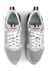 Šedé sportovní boty vyrobené z síťoviny a sveďového materiálu, bílé tkaničky, zelené vnitřní podrážky a tříbarevný poutko se červenými, bílými a modrými akcenty.