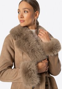 Abrigo beige con cuello de piel y puños, que presenta una textura suave, cierre de botones y un diseño estructurado.