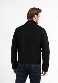 Sort jakke med krave, lavet af glat stof. Har sidelommer og lige snit. Bæres med mørkeblå denim jeans.