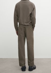 Brauner Strickpullover mit lockerer Passform und geripptem Saum, kombiniert mit lockeren braunen Hosen mit Gesäßtaschen. Schwarze klobige Schuhe runden den Look ab.