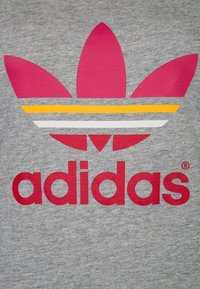 Grått tyg med en stor rosa trefoil-logotyp med tre bladformer och tre horisontella ränder i gult, vitt och grått under logotypen.