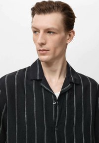 Zwarte gestreepte shirt met een kraag, gemaakt van gestructureerde stof. Kenmerkt lichtgrijze verticale strepen en een knoopsluiting aan de voorkant.