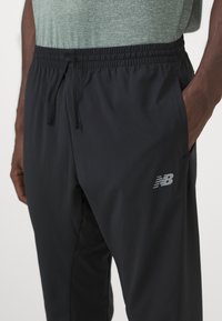 Schwarze Sporthose mit elastischem Bund, Kordelzug und Seitentaschen; mit einem kleinen grauen New Balance-Logo auf dem linken Oberschenkel.
