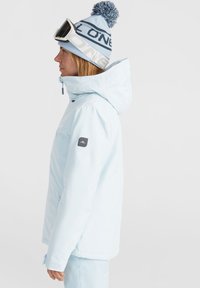 Lichtblauw skijack met kap, voorzien van een zwart logo op de mouw en witte ritsaccenten. Bijpassende blauwe beanie met pompon.