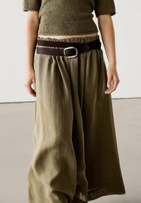 Groene gebreide top gecombineerd met een olijfgroene losse rok. De rok heeft een brede tailleband met een bruine leren riem en een zilveren gesp.