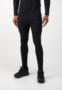 Svarte treningstights laget av elastisk, fukttransporterende stoff. Har en tettsittende design og glatt tekstur. Bært med svarte joggesko.