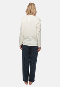 Krämfärgad pyjamaströja med långa ärmar och avslappnad passform, i kombination med marinblå byxor med prickar i mjukt tyg. Utmärkande detaljer inkluderar mudd och midjeresår.