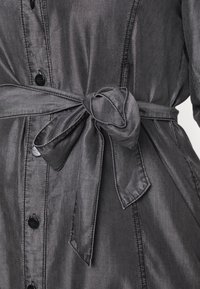 Grå denim skjortkjol med bälte i midjan, knappstängning och synliga sömmar. Materialet har en lätt lyster och en slät textur.