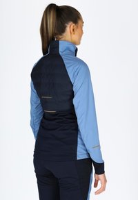 Fitted athletic jacket featuring a mix of light blue and navy fabric, with quilted texture on the upper back and gold accents.
