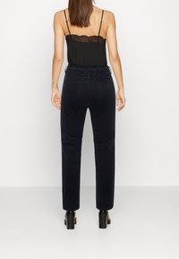 Marinblå manchesterbyxor med hög midja, raka ben och bakfickor. Stylar med en svart spetstopp och svarta klackskor.