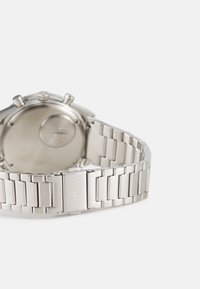 Silver stainless steel watch with a polished finish, featuring a textured link bracelet and a round case with crown and push buttons.