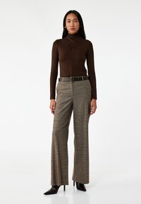 Top marrón de manga larga con cuello alto, combinado con pantalones de cuadros de pierna ancha. El conjunto incluye un cinturón oscuro y elegantes tacones negros.