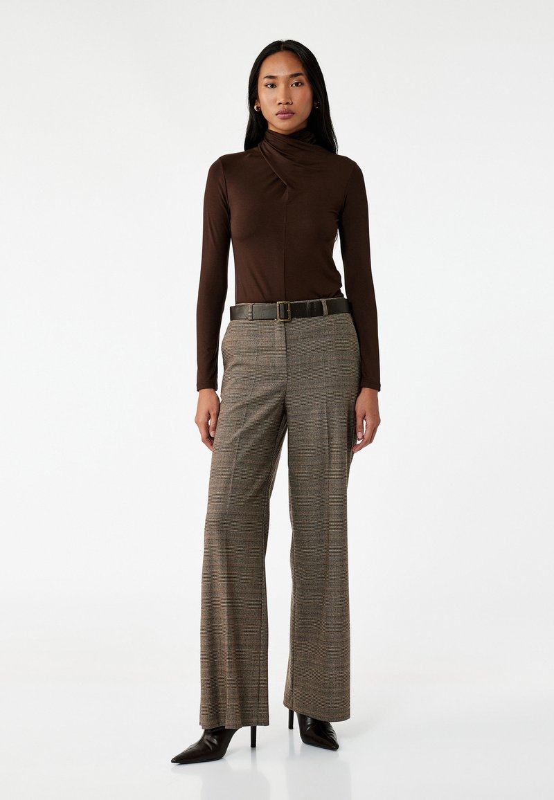 Top marrón de manga larga con cuello alto, combinado con pantalones de cuadros de pierna ancha. El conjunto incluye un cinturón oscuro y elegantes tacones negros.