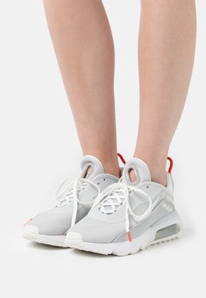 Lichtgrijze sportschoenen met witte accenten, van gaasachtig materiaal, een ronde neus, veters en een rode lip aan de hiel. Duidelijke luchtkussen zichtbaar.