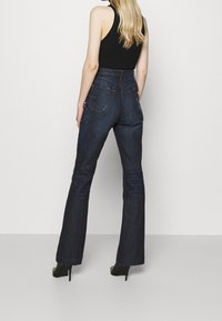 Högmidjade mörkblå jeans med utsvängd ben, med bakfickor och lätt vertikal sömdetaljer. I kombination med svarta högklackade skor.