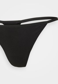 Čierne tangá s tenkými popruhmi, vyrobené z hladkého materiálu. Má minimalistický dizajn s nízkym pásom a bez viditeľného kovania.