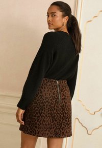 Pulover negru cu textură, asortat cu o fustă mini din material leopard maro, având un fermoar la spate. Întreaga ținută are o siluetă ajustată.