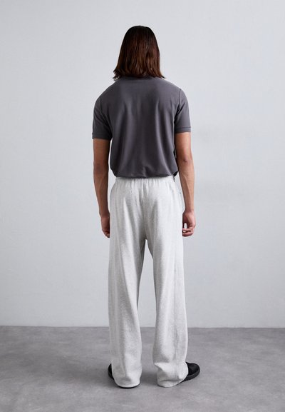Gray short-sleeve polo, relaxed fit, paired with loose, light gray trousers. Smooth fabric with an elastic waistband, black footwear.