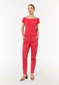 Czerwona bluzka bez ramion w połączeniu z czerwonymi wąskimi spodniami. Modelka ma na sobie beżowe szpilki. Gładki materiał, prosty krój i minimalistyczny design.