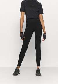 Cropped top atletico nero con maniche corte, abbinato a leggings neri a vita alta. Guanti neri senza dita e scarpe da corsa completano il look.