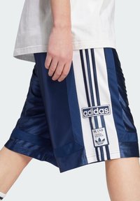 Calções de desporto azul marinho com painéis em malha, três riscas brancas e etiqueta com o logótipo da Adidas. Apresentam uma textura suave e um tecido contrastante.