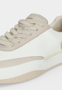 Gros plan d'une basket Geox beige et blanche avec des lacets en tissu, un col rembourré et une semelle extérieure blanche texturée.