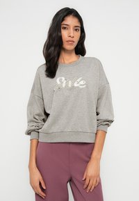 Γκρι φούτερ με άνετη εφαρμογή, με υφή σχεδίασης "Smile" σε λαμπερά στοιχεία. Μακριά μανίκια και ριμπ τελειώματα ολοκληρώνουν την εμφάνιση.