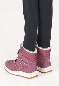 Les bottes violettes imperméables présentent une finition texturée, un col en fourrure, des sangles ajustables et une semelle en caoutchouc contrastante pour une meilleure traction.