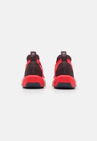 Des chaussures de sport rouges et bordeaux avec un dessus en tricot, des pattes de tirage et une semelle épaisse et texturée avec une base grise contrastante.