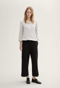 Blusa grigio chiaro con un motivo sottile, colletto e maniche tre quarti, abbinata a pantaloni neri a gamba larga e scarpe nere.