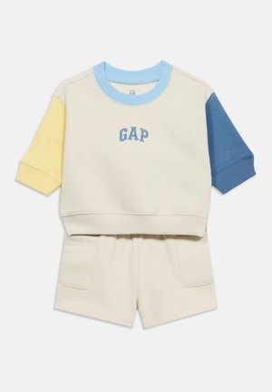 Σετ ρούχων για μικρό παιδί σε κρεμ χρώμα με φούτερ κοντομάνικο που έχει κίτρινες και μπλε μανίκια και ταιριαστό σορτς με μπροστινές τσέπες.