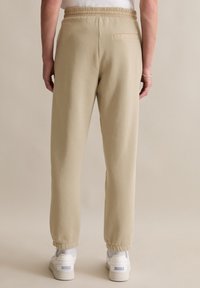 Licht beige sweatpants met een elastische tailleband, taps toelopende boorden en een achterzak, gecombineerd met witte sneakers. Zachte, gladde textuur.