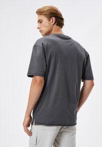 Camiseta gris de manga corta con un ajuste relajado, detalles de costura visibles y cuello redondo. La tela parece suave con una textura ligeramente desgastada.