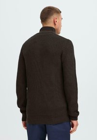 Mokka-farbener Strickpullover mit hohem Kragen, langen Ärmeln und gerippter Textur. Bietet einen lässigen Schnitt und einen verlängerten hinteren Saum.