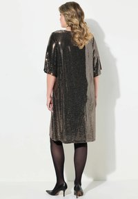 Schwarz-goldenes Paillettenabendkleid mit kurzen, breiten Ärmeln, lockerer Passform und gerader Silhouette, kombiniert mit schwarzen semi-opaque Strumpfhosen und Absatzschuhen.
