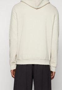 Sudadera con capucha beige de tejido suave, con mangas largas y dobladillo acanalado, combinada con pantalones negros holgados.