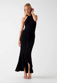 Robe noire à col licou avec fronces, détail volanté sur le côté et fente haute. Tissu lisse et extensible, silhouette ajustée.